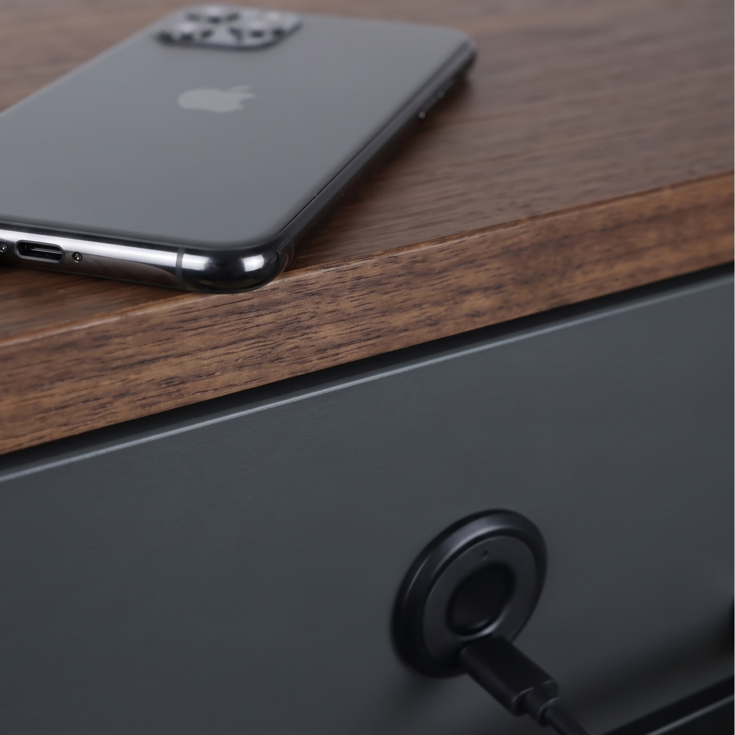 Serrure BORE LOCK installée sur un tiroir sombre, avec un smartphone posé à proximité sur un plan en bois, câble de charge USB-C branché